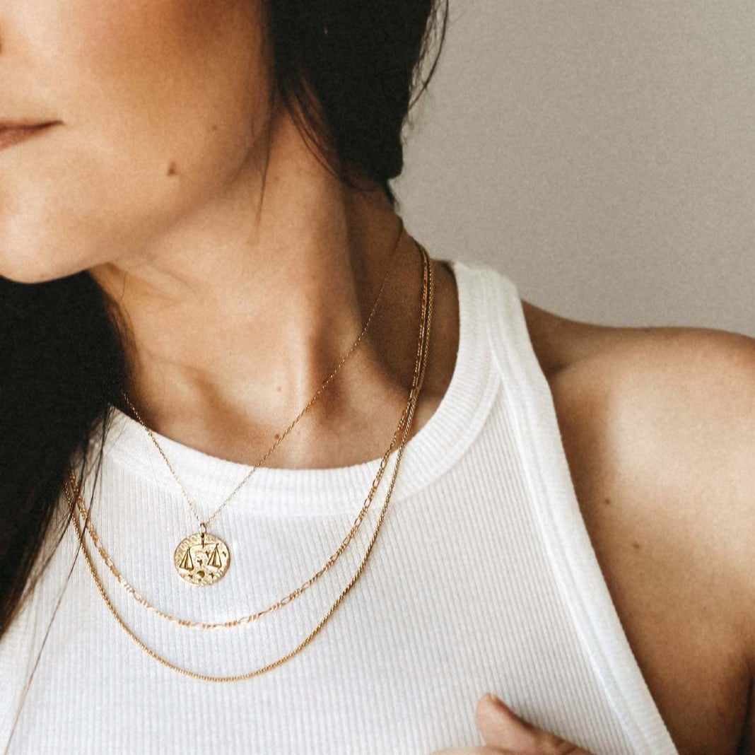 Collier Balance en plaquĂ© or 18 carats portĂ© par une femme, pendentif rond gravĂ© du symbole Balance entourĂ© dâĂ©toiles, bijou fĂ©minin raffinĂ© et lumineux. IdĂ©e cadeau femme.
