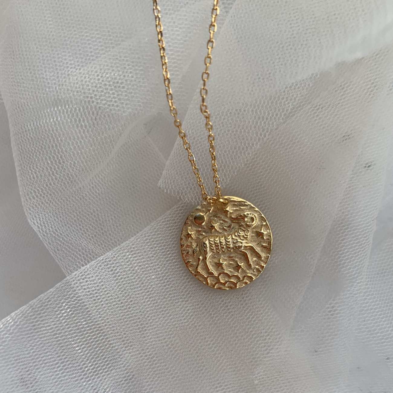 Collier Bélier doré posé sur du tulle blanc, médaillon gravé représentant le signe astrologique du Bélier. Idée cadeau femme.