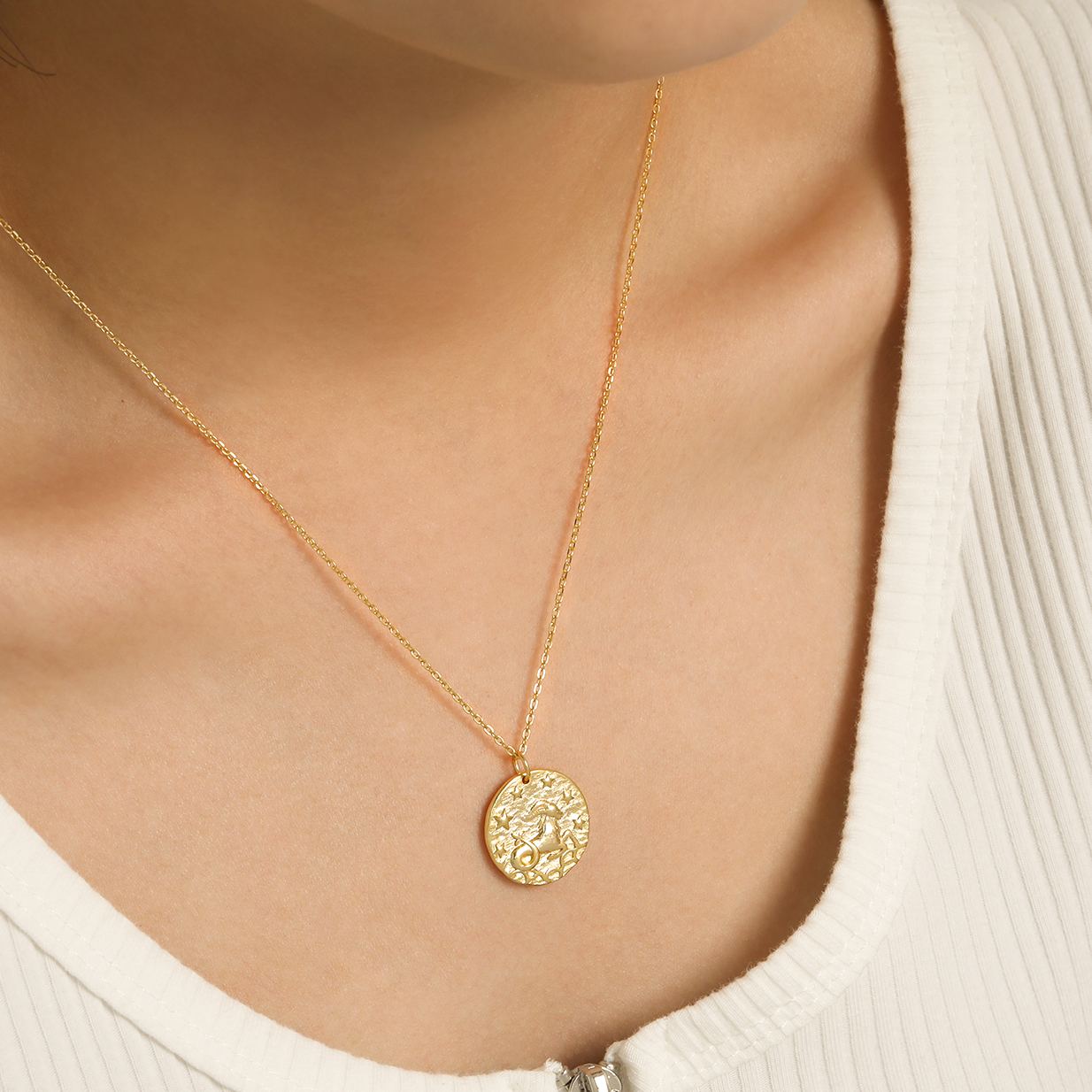 Collier en or plaqué avec pendentif Capricorne porté autour du cou, design astrologique raffiné sur fond de haut blanc cÎtelé. Idée cadeau femme.