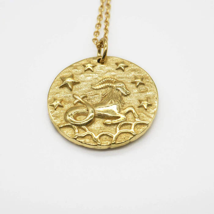 Gros plan sur un pendentif doré représentant le signe astrologique du Capricorne, avec étoiles en relief sur fond doré. Idée cadeau femme.