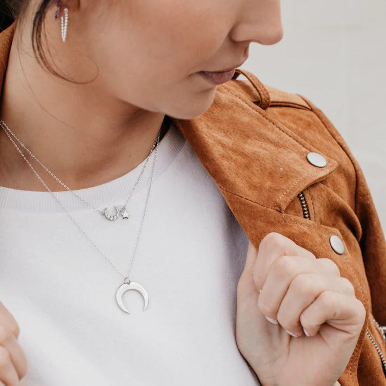 Femme portant un collier lune en argent 925, look moderne avec veste camel et tee-shirt blanc, idée cadeau.