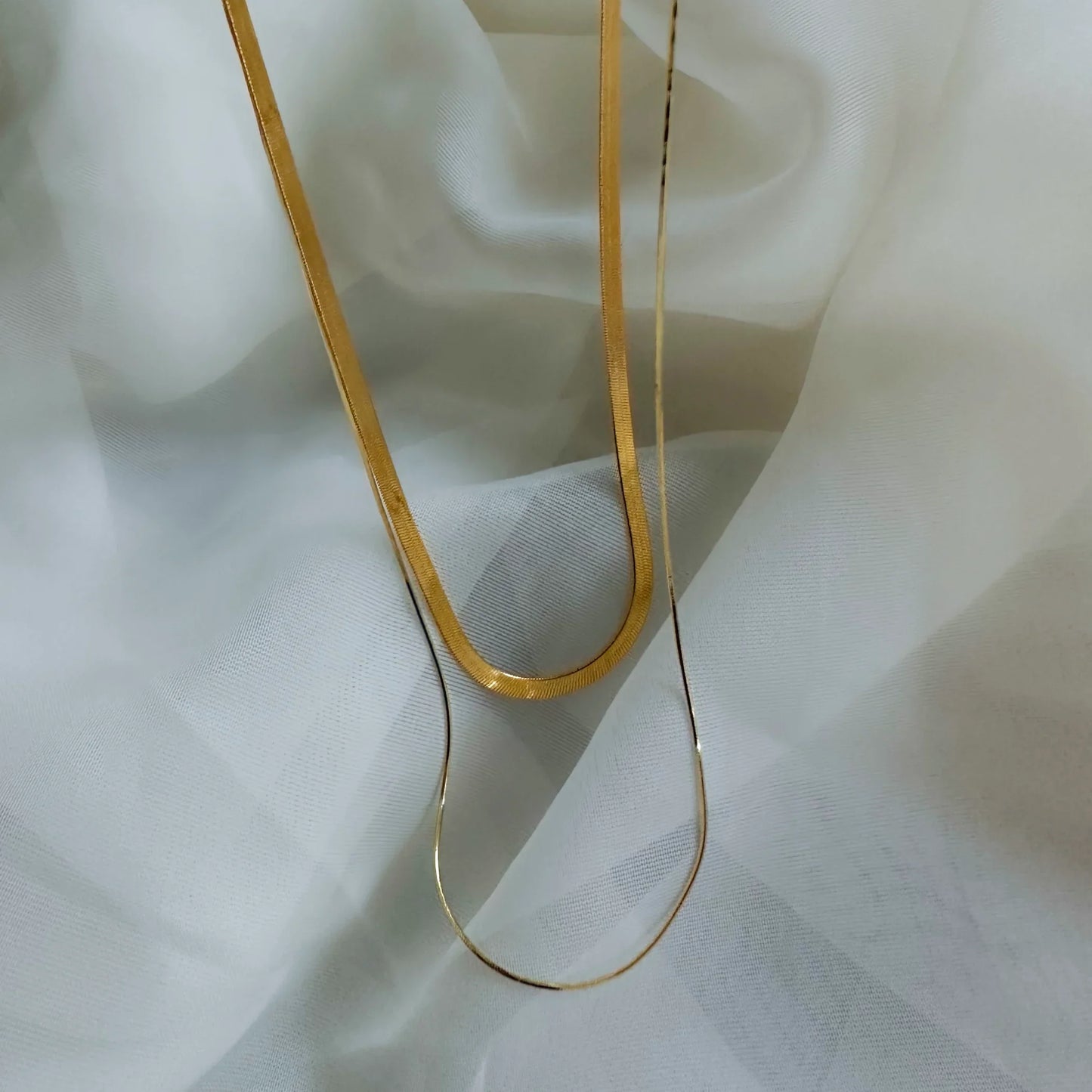 Collier doré chaîne plate ondulée posé sur un tissu blanc fluide. Idée cadeau, koolkado