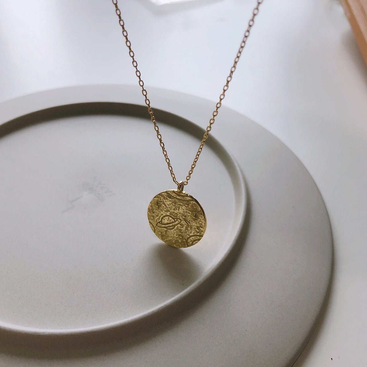 Collier doré avec pendentif planÚtes posé élégamment sur une assiette. Idée cadeau femme.