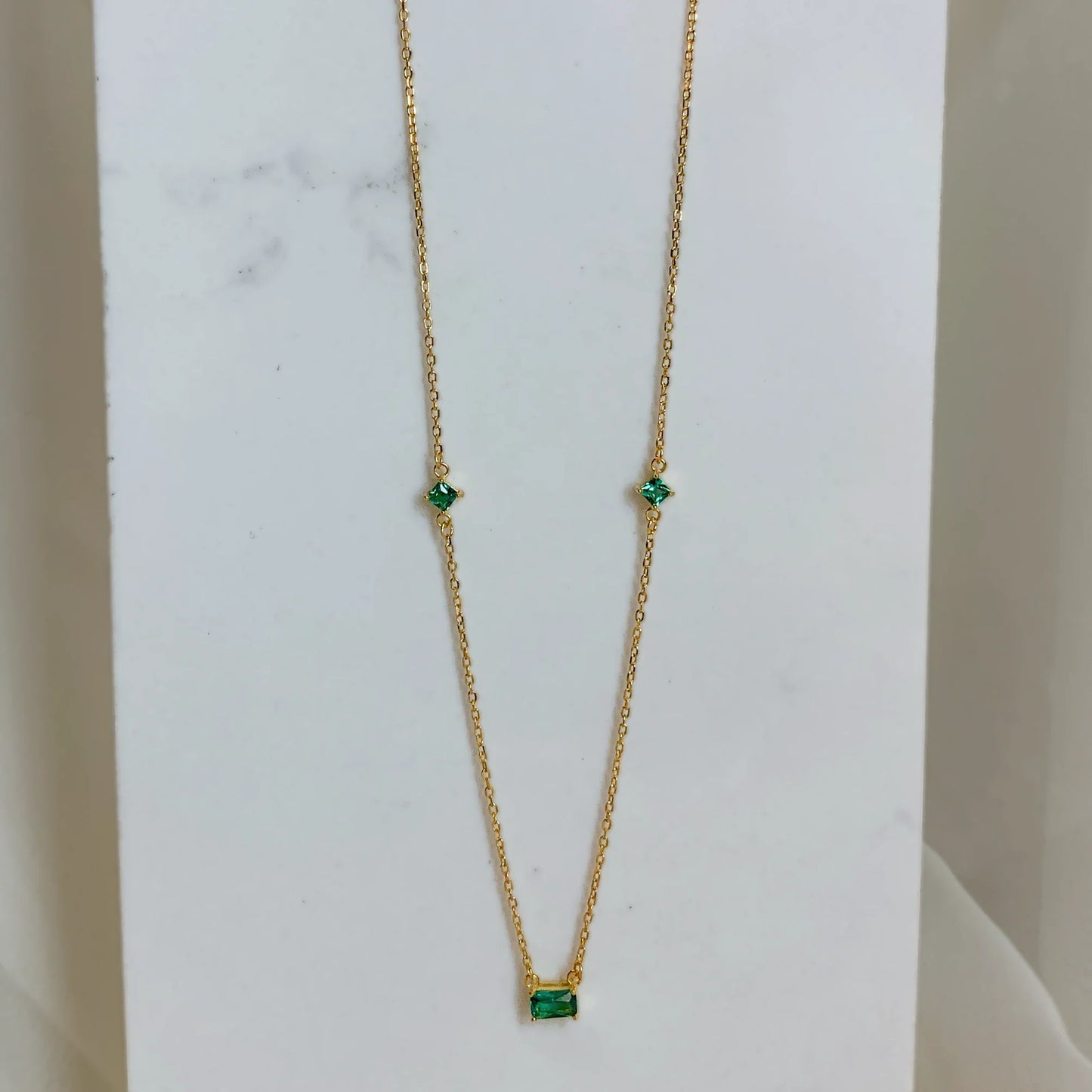 Collier doré avec pierre verte posé verticalement sur un fond marbré blanc. Idée cadeau femme, collier romy, koolkado.be