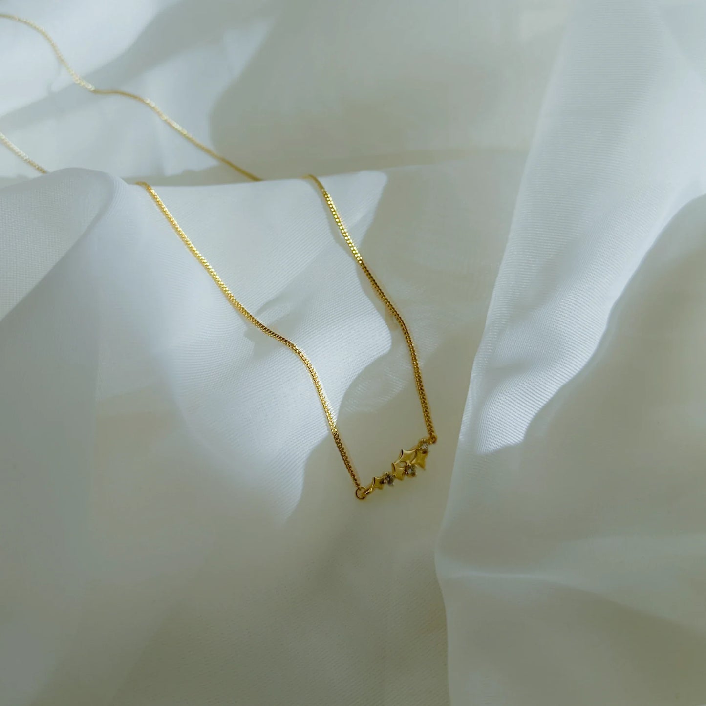 Collier Astrid doré avec étoiles brillantes posé sur tissu blanc – Idées cadeau femme, koolkado