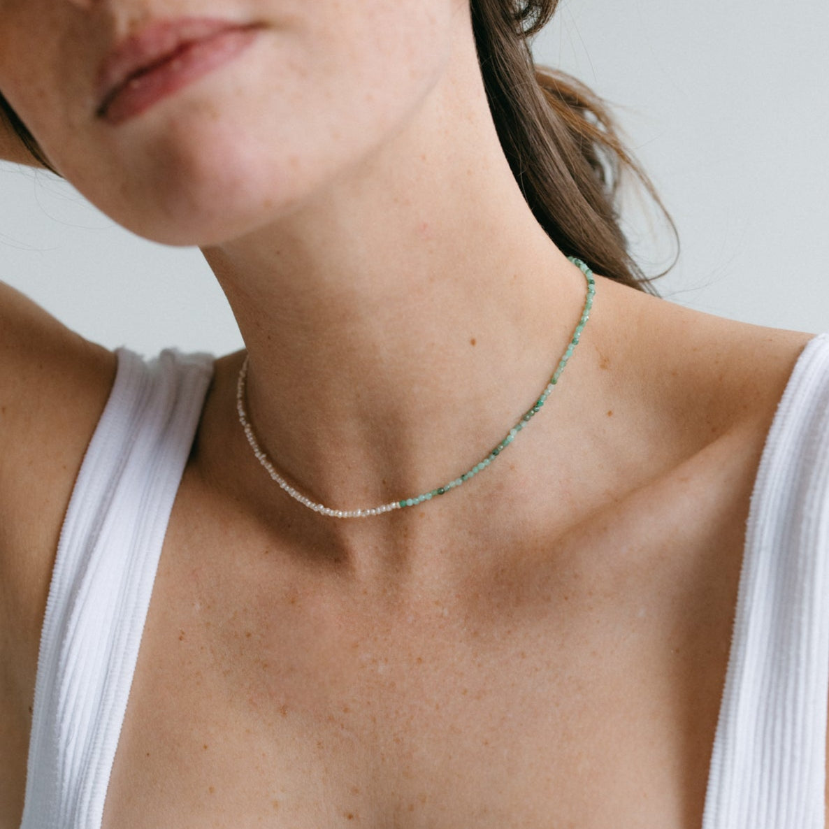 Femme élégante portant le collier Emmie en perles de culture et pierres émeraude, bijou fait main, style minimaliste en débardeur blanc, idée cadeau femme.