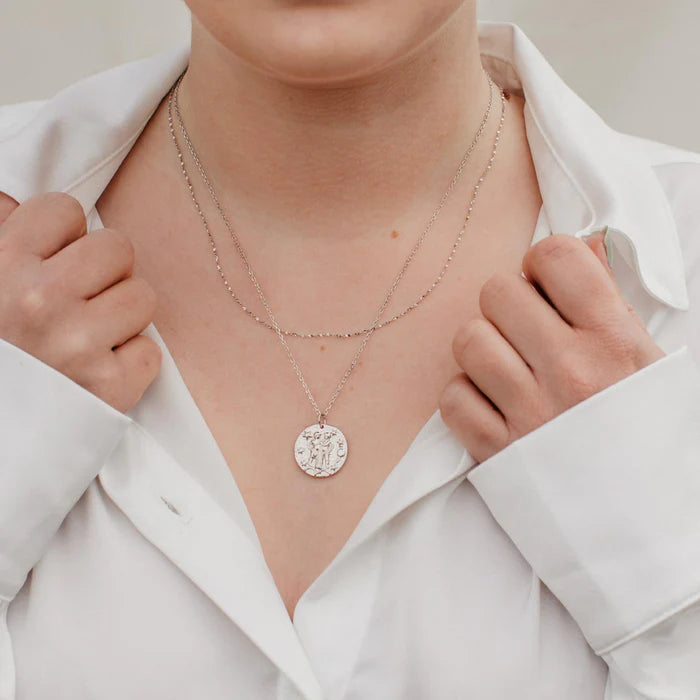 Femme portant un collier en argent sterling avec pendentif zodiaque Gémeaux deux personnages enlacés fond étoilé. Idée cadeau femme.