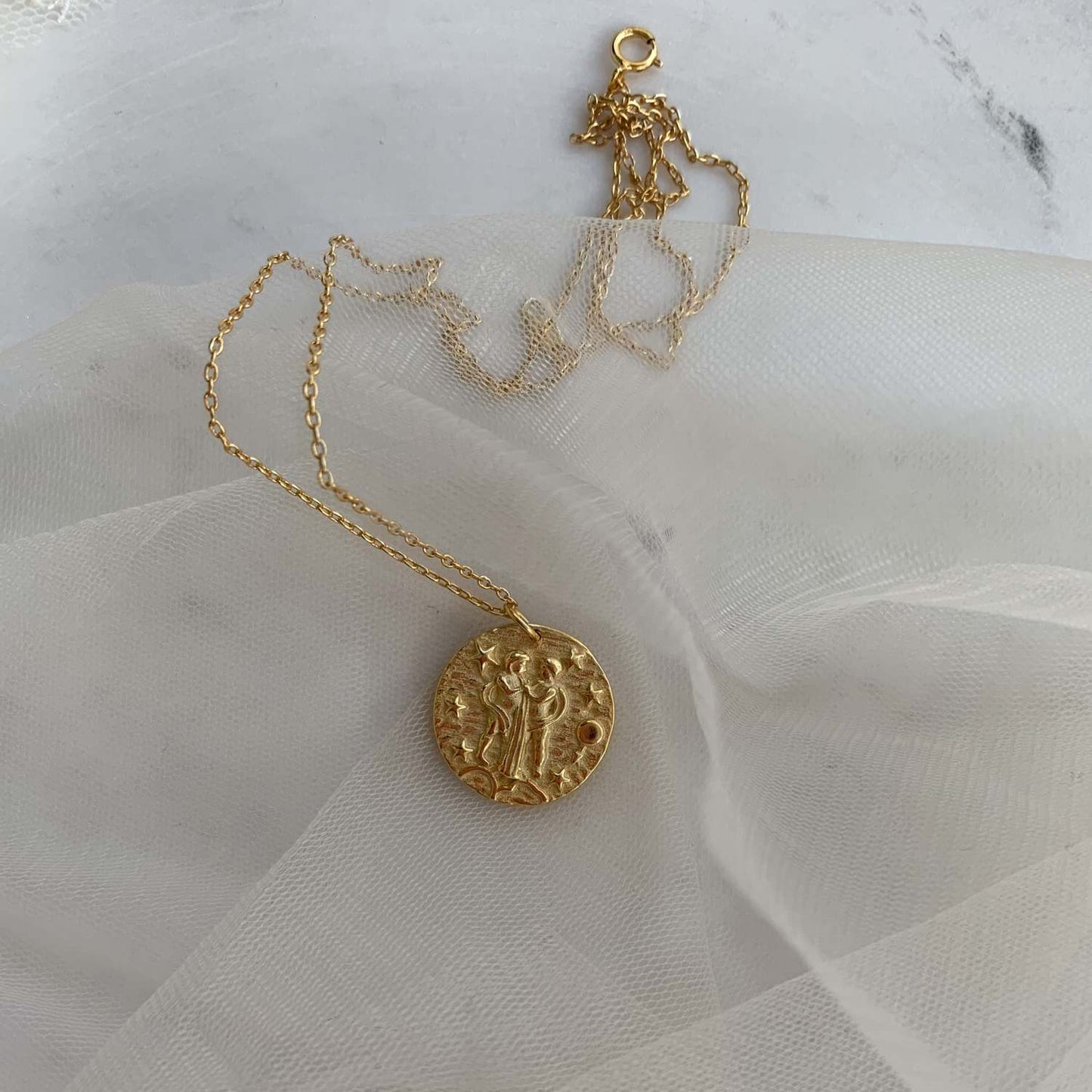 Collier pendentif Gémeaux en plaqué or 18 carats avec symbole zodiaque représentant deux personnages, sur fond étoilé. Idée cadeau femme.