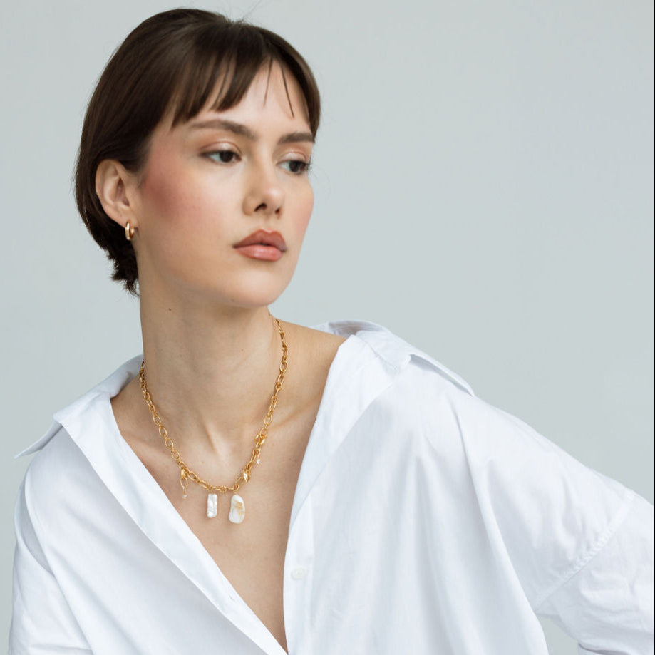 Femme élégante portant un collier grigri en plaqué or avec pendentifs naturels, bijou bohème chic fait main, porté avec une chemise blanche, idée cadeau femme.