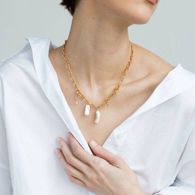 Gros plan sur un collier grigri en plaqué or porté par une femme, avec pendentifs perles naturelles et coquillages, bijou artisanal au style bohème chic, idée cadeau femme.