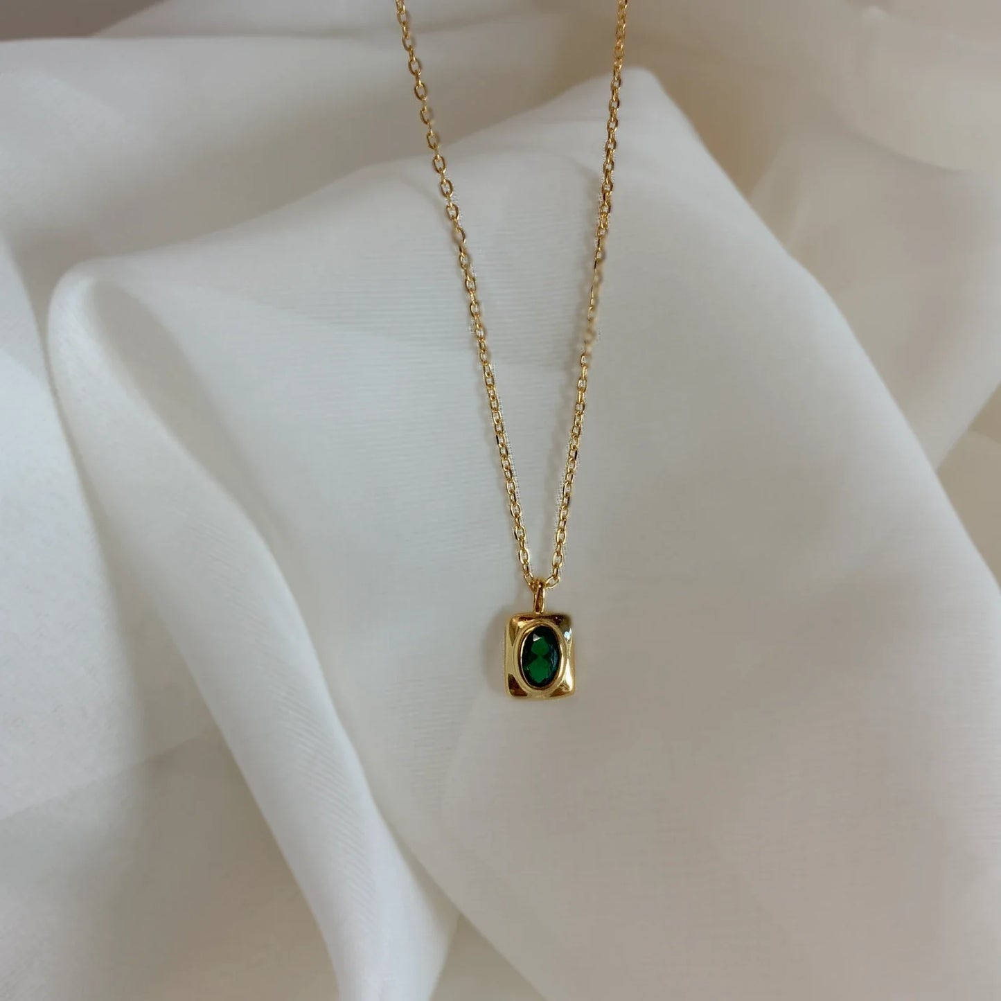 Gros plan du collier Kalea posĂ© sur tissu blanc, pierre Ă©meraude visible â IdĂ©es cadeau femme, collier Kalea Love Local Jewelry, koolkado