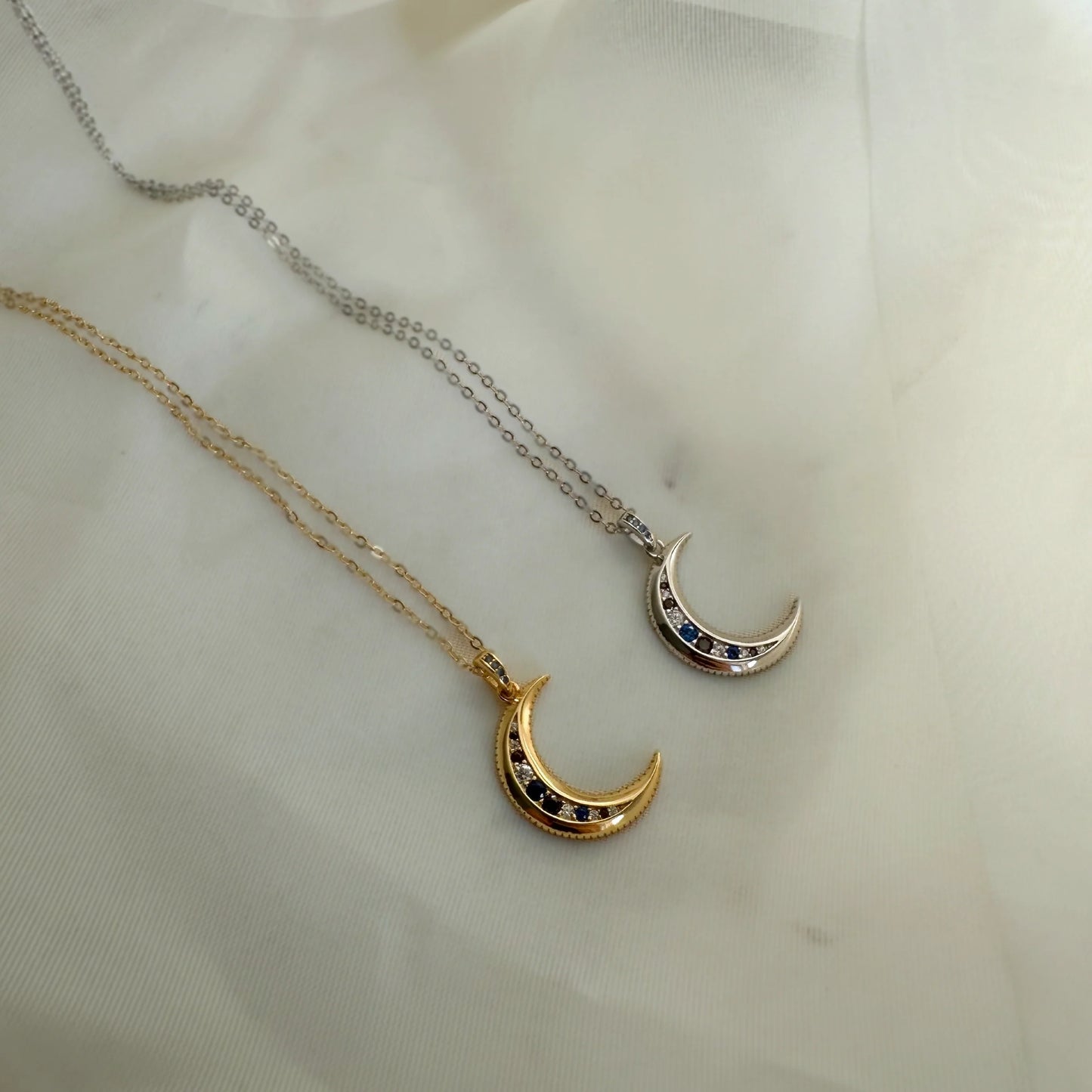 Deux colliers pendentif lune, version dorée et argentée, posés à plat sur tissu blanc. Idée cadeau femme.