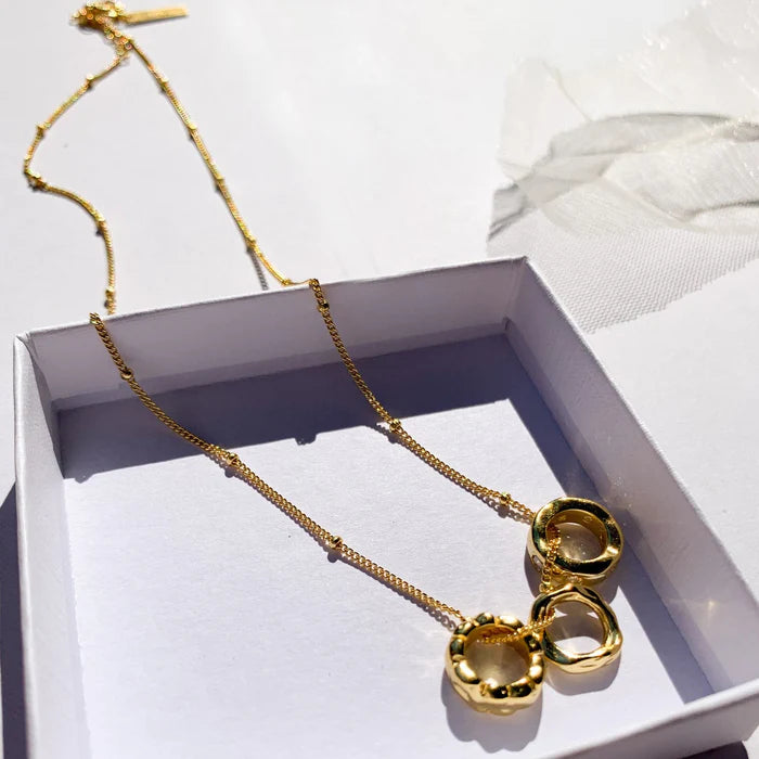 Collier doré Malou dans un coffret cadeau blanc exposé au soleil. Idée cadeau femme.