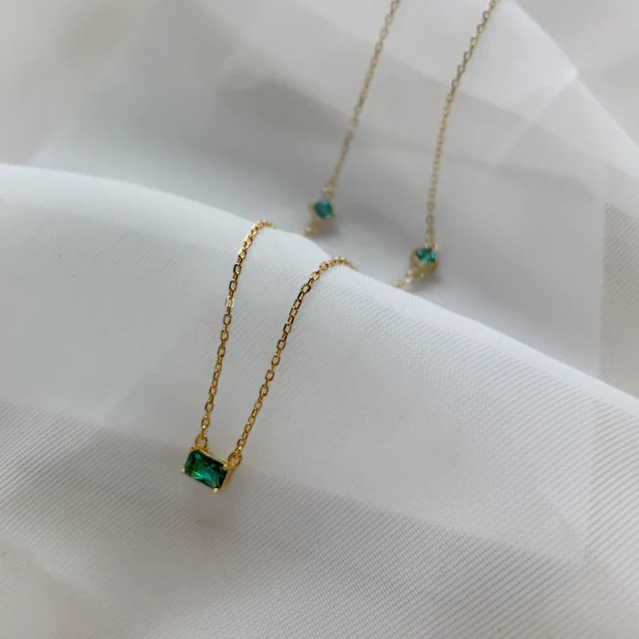 Gros plan sur un collier doré à pierre verte, posé sur un tissu blanc. Idée cadeau, collier Romy, koolkado.