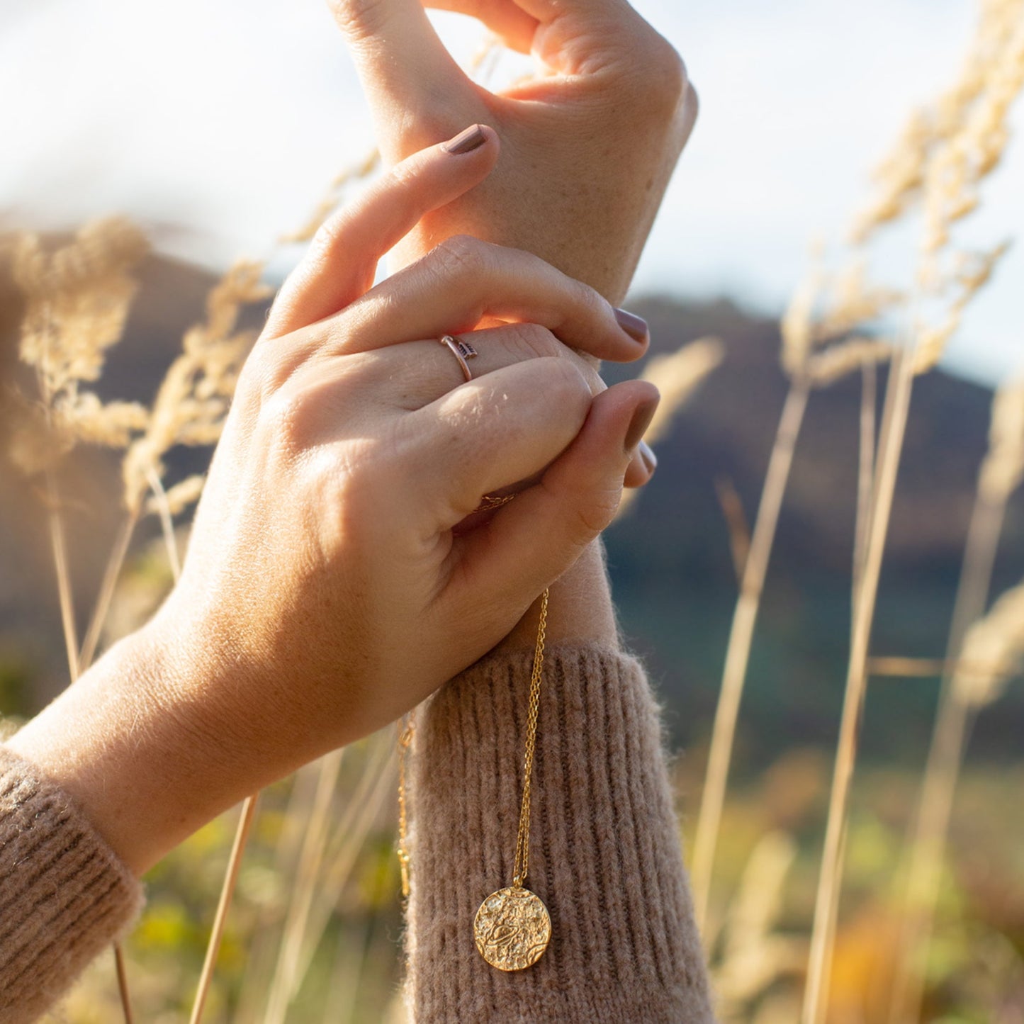 Mains tenant un collier doré dans un champ lumineux, ambiance naturelle et chaleureuse. Idée cadeau femme.
