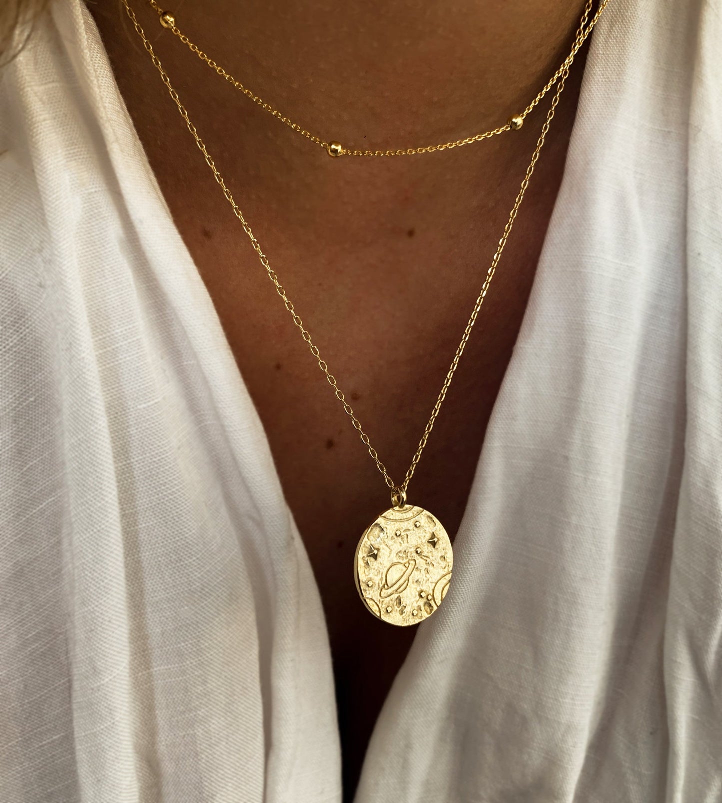 Collier superposé porté avec un décolleté, mettant en valeur un pendentif doré à motif cosmique. Idée cadeau femme.