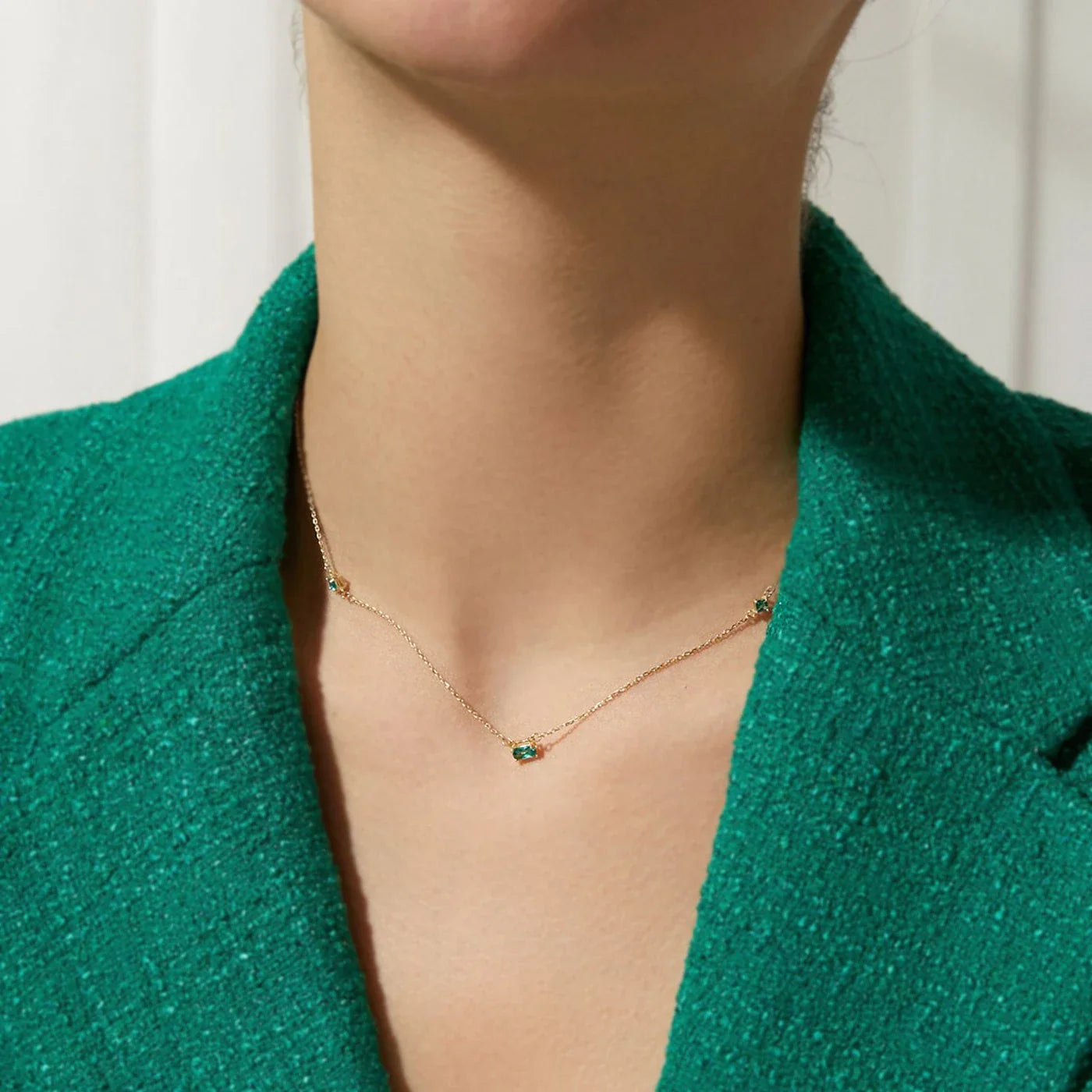 Collier doré à pierre verte porté par une femme en veste verte élégante. Idée cadeau femme. Collier Romy, koolkado.be