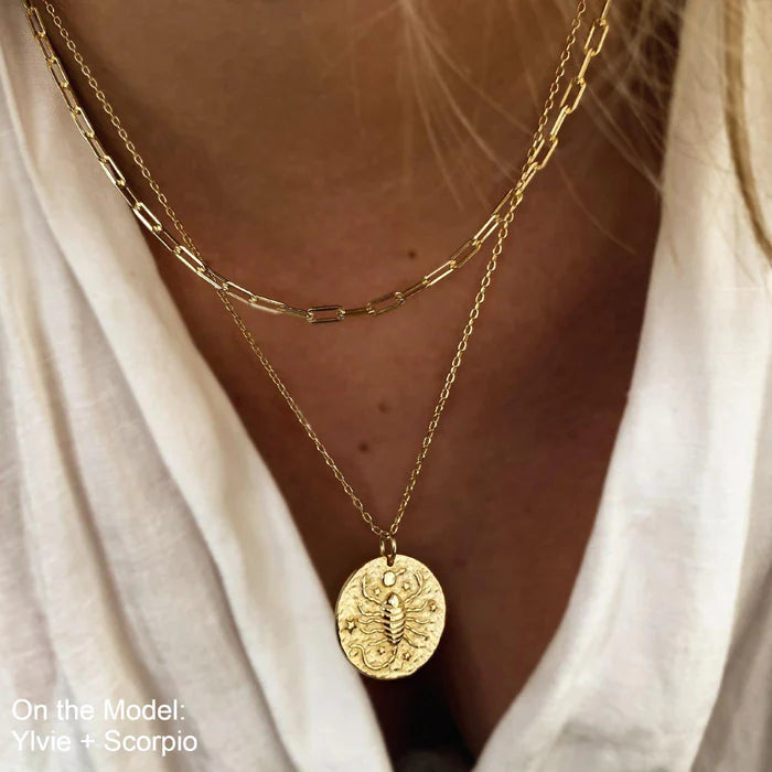 Collier Scorpion en plaquĂ© or 18 carats portĂ© en double chaĂźne par une femme, pendentif rond gravĂ© dâun scorpion entourĂ© dâĂ©toiles, look tendance et Ă©lĂ©gant avec superposition de bijoux. IdĂ©e cadeau femme.