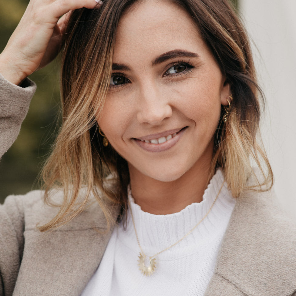 Femme souriante portant un collier doré soleil, bijou chic et lumineux au style moderne, idée cadeau femme.
