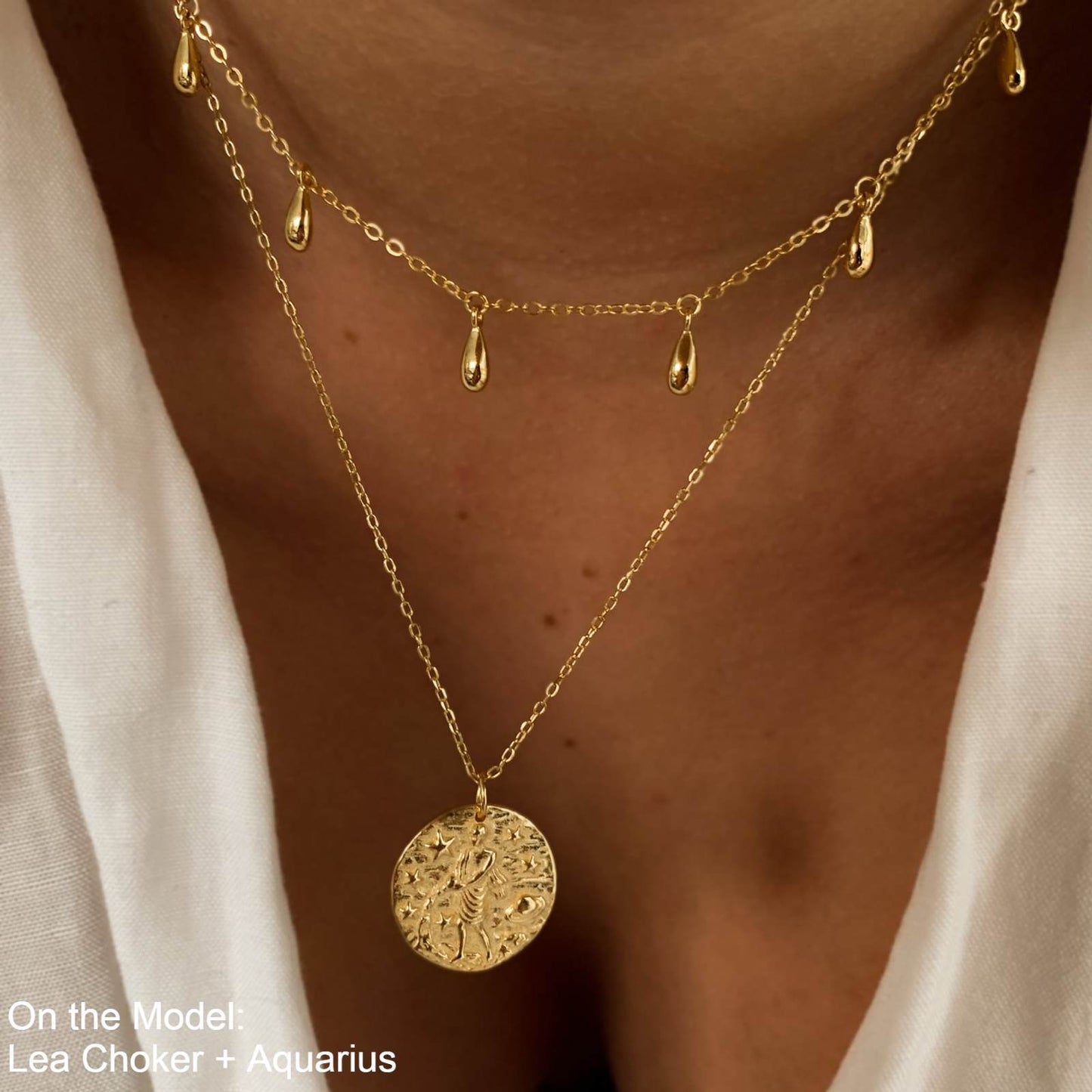 Collier Verseau en plaquĂ© or 18 carats portĂ© en double chaĂźne par une femme, pendentif rond gravĂ© dâun verseau entourĂ© dâĂ©toiles et planĂštes, bijou fĂ©minin Ă©lĂ©gant avec superposition de chaĂźnes et gouttes. IdĂ©e cadeau femme.