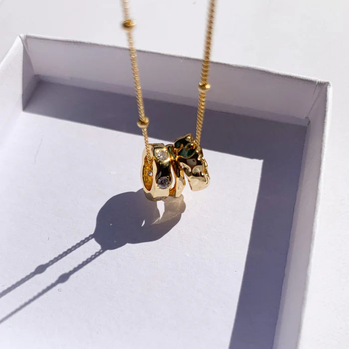 Gros plan sur les pendentifs sculptés du collier Malou dans leur boîte. Idée cadeau femme.