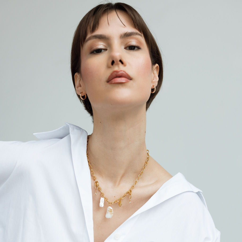 Femme portant un collier grigri en plaqué or avec pendentifs perle et coquillage, bijou artisanal au style bohème chic, look élégant et minimaliste, idée cadeau femme.