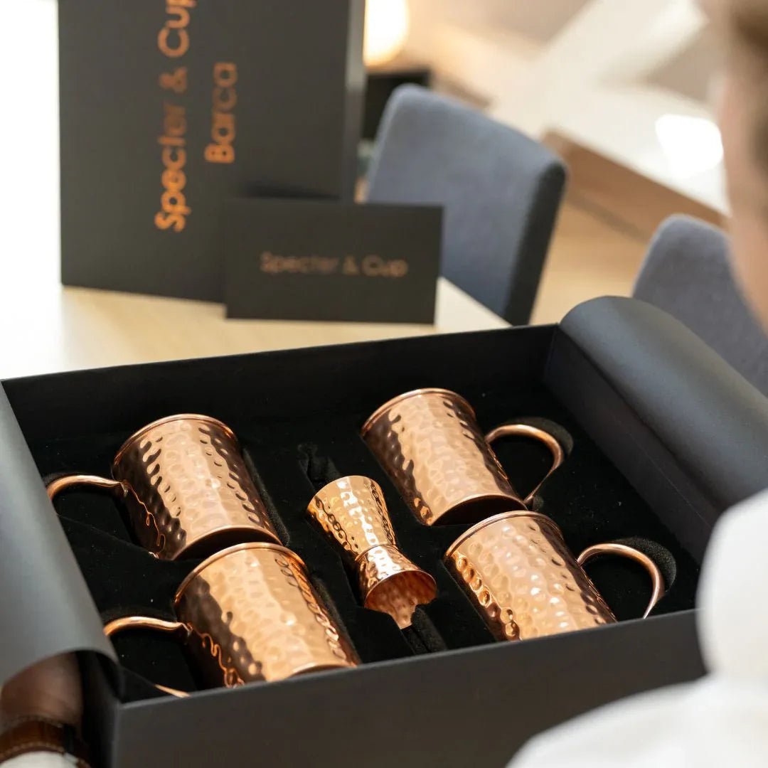 Vue de dessus du coffret Barca ouvert revelant les 4 mugs en cuivre massif et les accessoires de mixologie soigneusement ranges dans leur ecrin