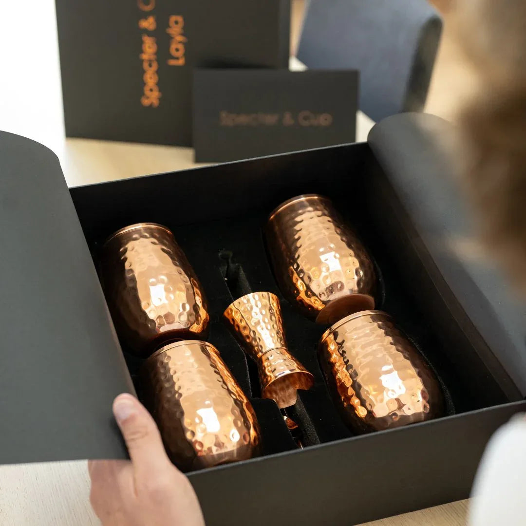 Vue de dessus du coffret Layla ouvert revelant les 4 gobelets galbes en cuivre massif et les accessoires de mixologie ranges dans leur ecrin