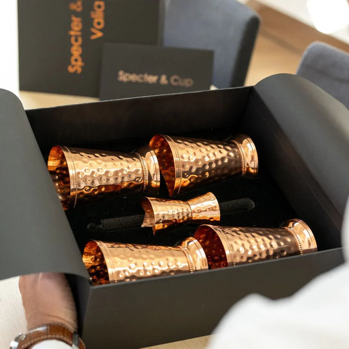 Vue plongeante du coffret Valia ouvert revelant les 4 gobelets sculptes en cuivre massif et les accessoires de mixologie ranges dans leur ecrin