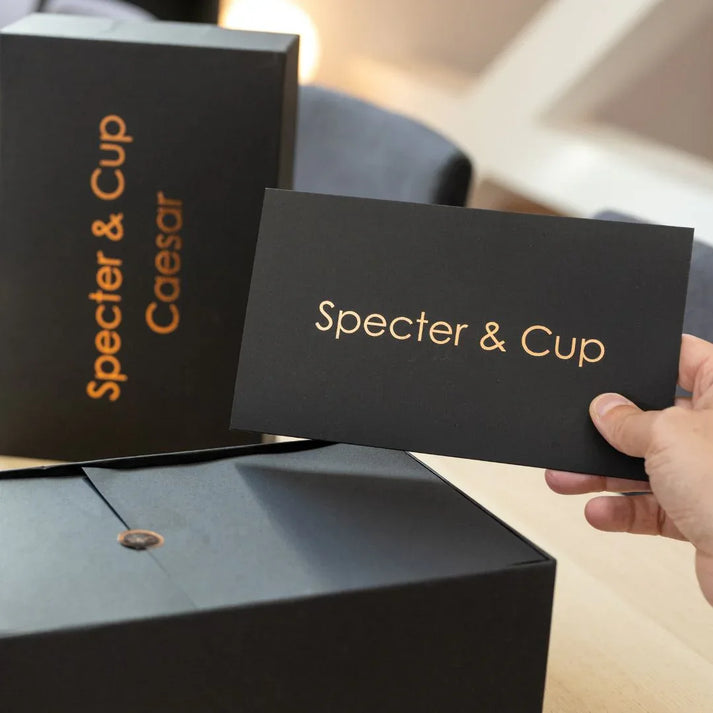 Carte Specter & Cup présentée à la main devant un coffret cadeau premium, détail du packaging prêt à offrir – idée cadeau – KoolKado

