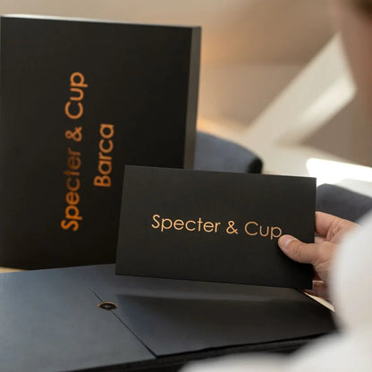 Main tenant la carte de bienvenue Specter et Cup devant le coffret de luxe Barca illustrant un emballage haut de gamme exclusif