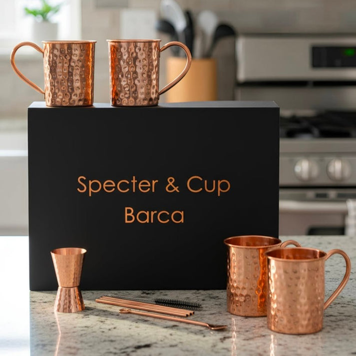 Set complet Moscow Mule Barca en cuivre pur martele avec 4 mugs pailles doseur et cuillere devant son coffret cadeau noir haut de gamme