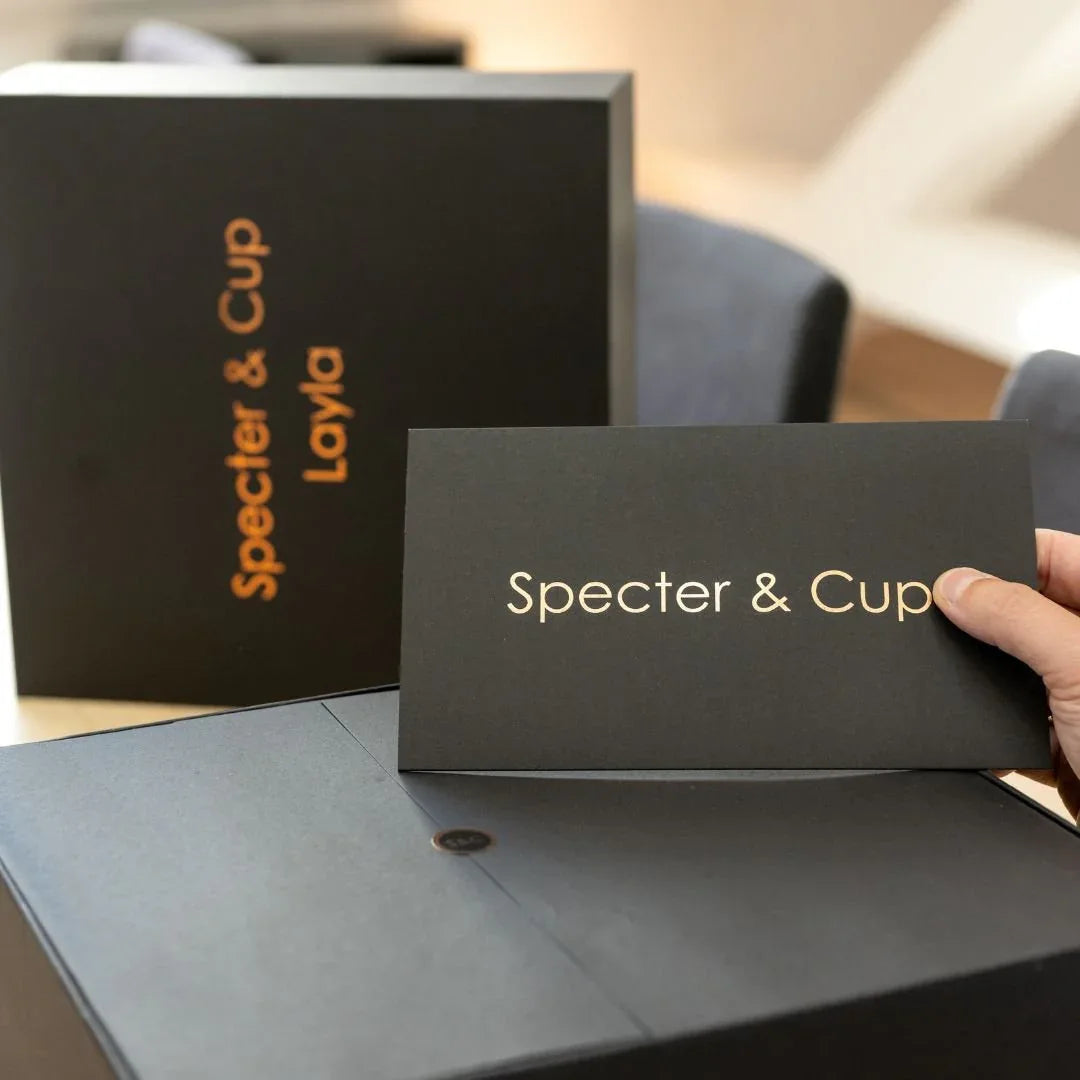 Main tenant la carte de bienvenue Specter et Cup devant le coffret de luxe Layla illustrant un emballage haut de gamme exclusif