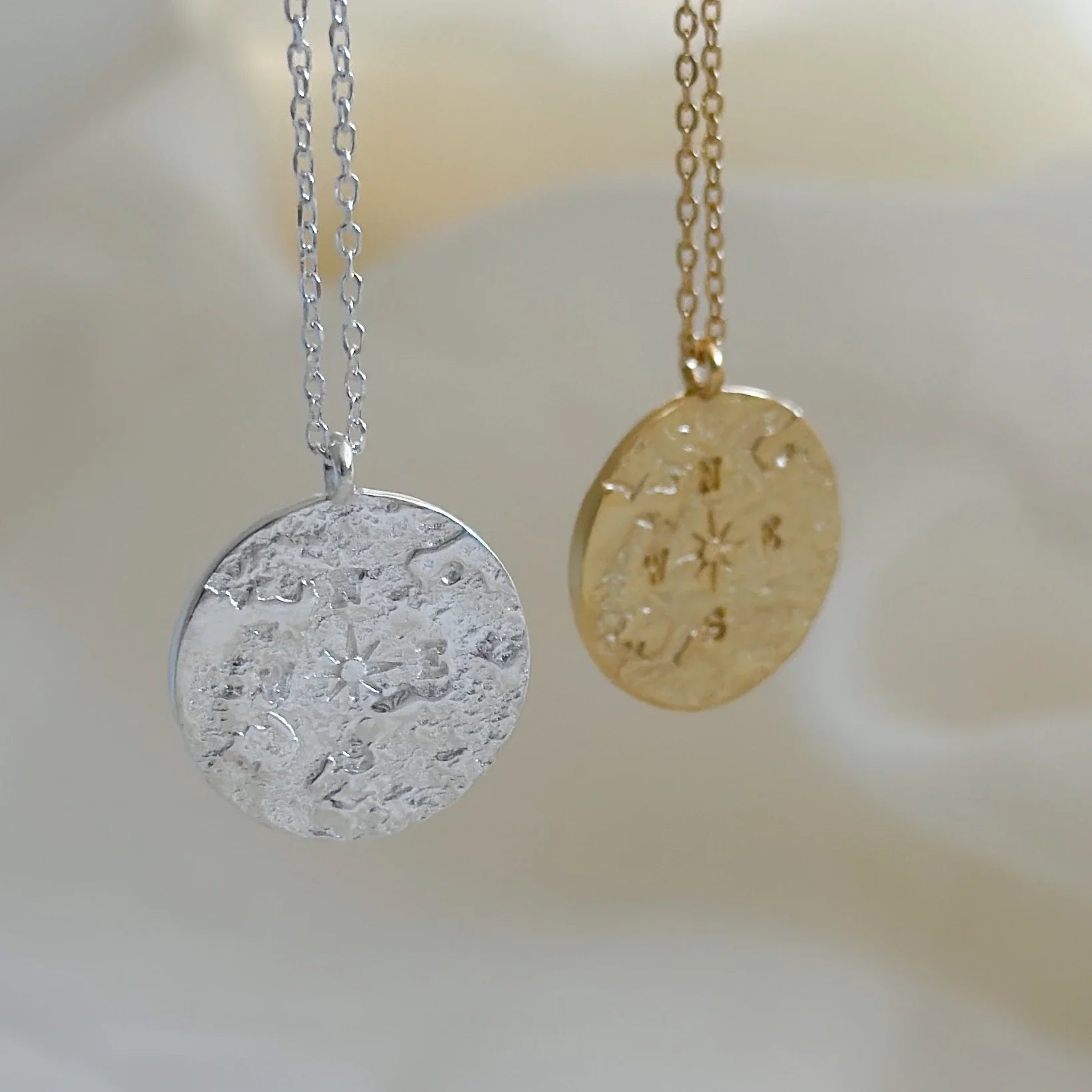Médaillons boussole suspendus, en argent et doré, sur fond doux. Collier atlas love local jewelry. Koolkado.