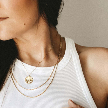 Collier Balance en plaqué or 18 carats porté par une femme, pendentif rond gravé du symbole Balance entouré d’étoiles, bijou féminin raffiné et lumineux. Idée cadeau femme.
