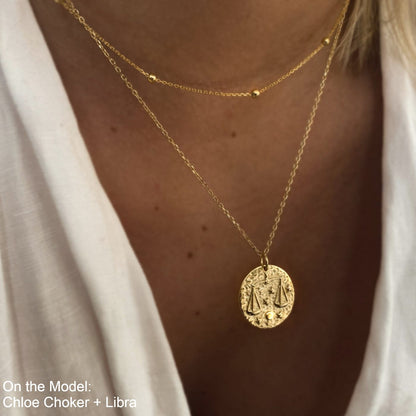 Collier Balance en plaqué or 18 carats avec pendentif rond gravé du symbole Balance et étoiles, porté sur un cou féminin, bijou élégant et raffiné. Idée cadeau femme.