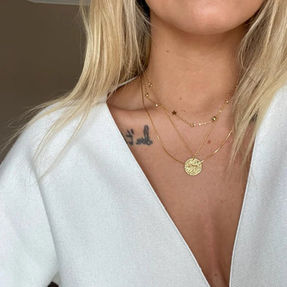Femme portant un collier Bélier doré avec deux autres chaînes fines à breloques étoiles, style astrologie chic. Idée cadeau femme.