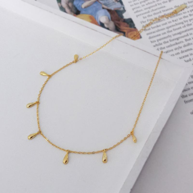 Collier Lea doré avec pampilles goutte photographié sur un livret. Idée cadeau femme. Koolkado.