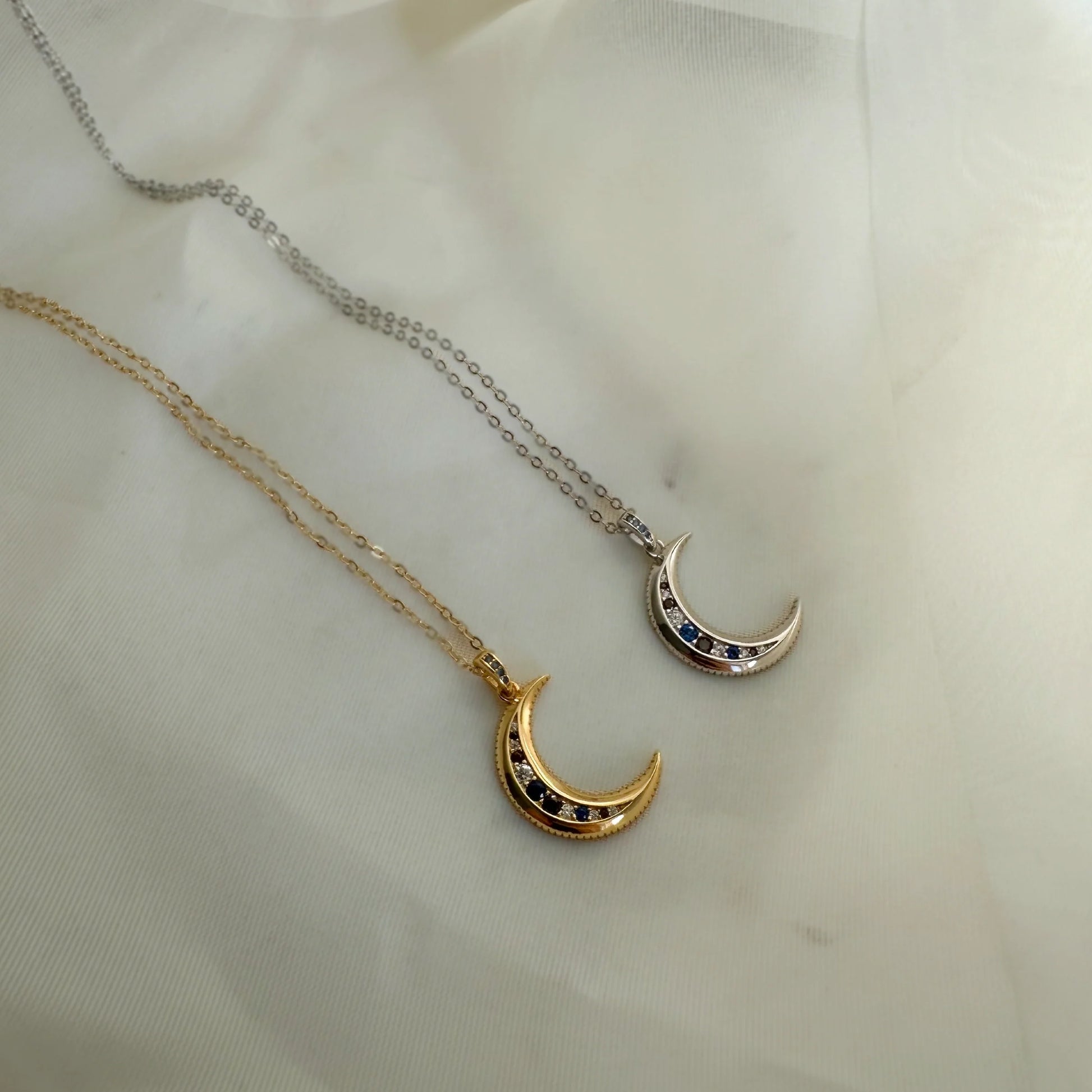 Deux colliers pendentif lune, version dorée et argentée, posés à plat sur tissu blanc. Idée cadeau femme.