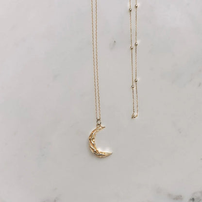 Collier Matea doré avec pendentif croissant de lune posé sur fond marbre – Idées cadeau femme, collier Matea Love Local Jewelry, koolkado