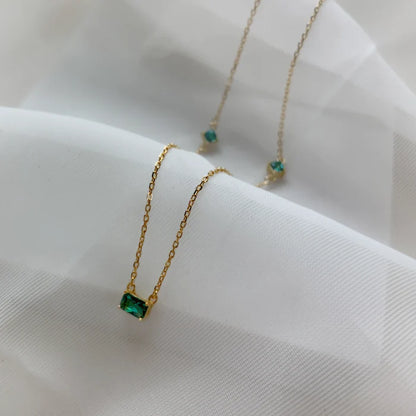 Gros plan sur un collier doré à pierre verte, posé sur un tissu blanc. Idée cadeau, collier Romy, koolkado.