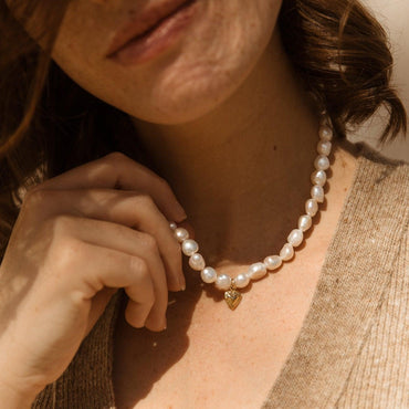 Femme portant un collier ras-du-cou en perles baroques avec pendentif cœur doré. Idée cadeau femme ou ado.