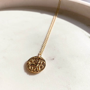Collier Sagittaire en plaqué or 18 carats avec pendentif rond gravé d’un centaure avec arc, entouré d’étoiles, bijou féminin élégant posé sur surface claire. Idée cadeau femme.