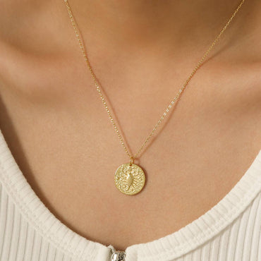 Collier Scorpion en plaqué or 18 carats porté par une femme, pendentif rond texturé gravé d’un scorpion, chaîne fine élégante, bijou féminin raffiné porté sur peau claire. Idée cadeau femme.
