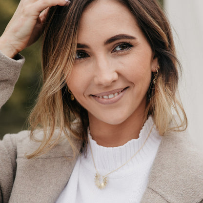 Femme souriante portant un collier doré soleil, bijou chic et lumineux au style moderne, idée cadeau femme.