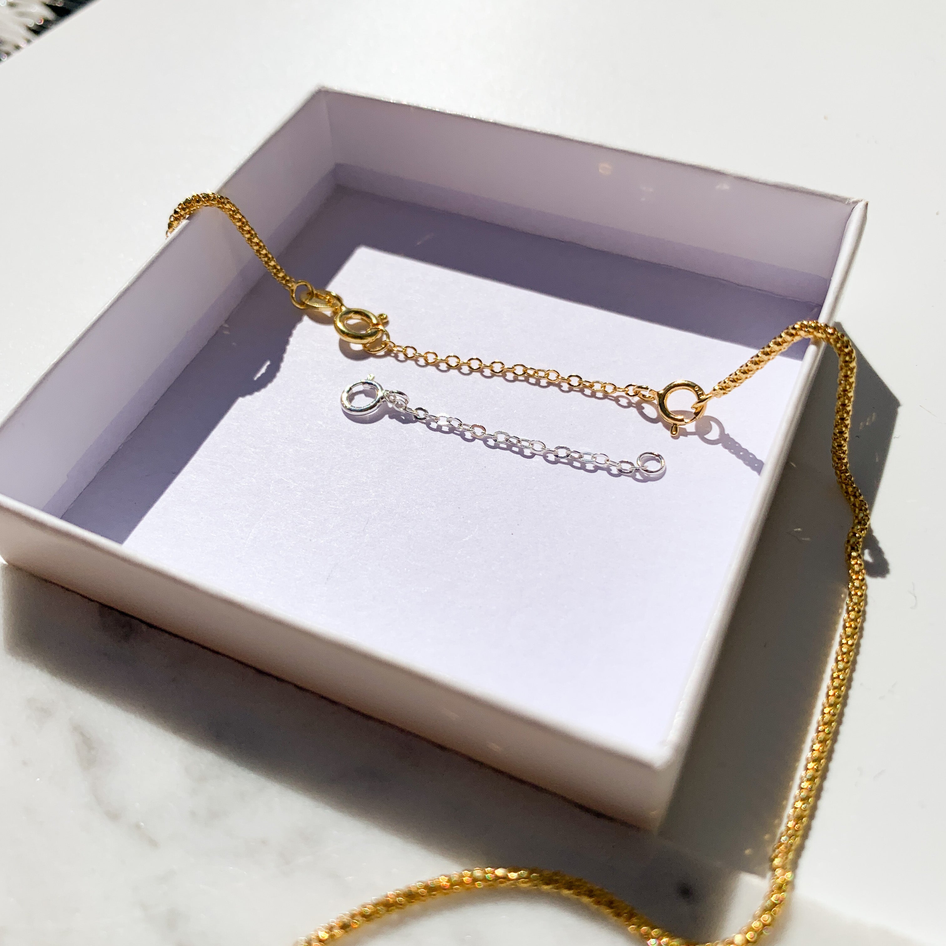 Chaînes d’extension attachées à un collier doré dans une boîte cadeau, vue en gros plan éclairée. Idée cadeau femme.