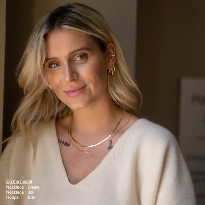 Femme blonde souriante portant un collier snake chain et des boucles dorées. Idée cadeau femme. Koolkado.
