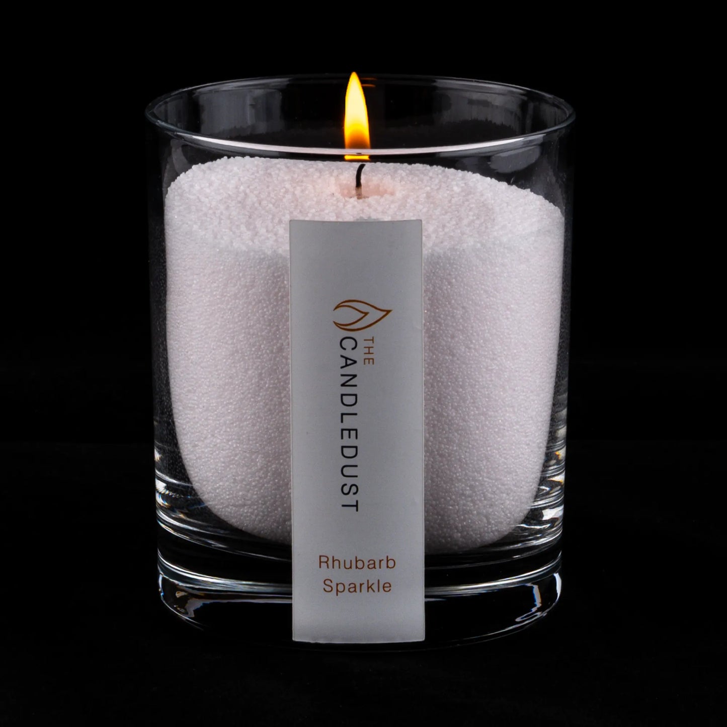 Idées cadeaux pour adulte : bougie parfumée Champagne & Rhubarbe Candledust allumée, mise en valeur sur fond sombre élégant