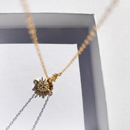 Idées cadeaux pour femme : collier double pendentif soleil présenté dans sa boîte cadeau, capturant la lumière pour un effet poétique et raffiné