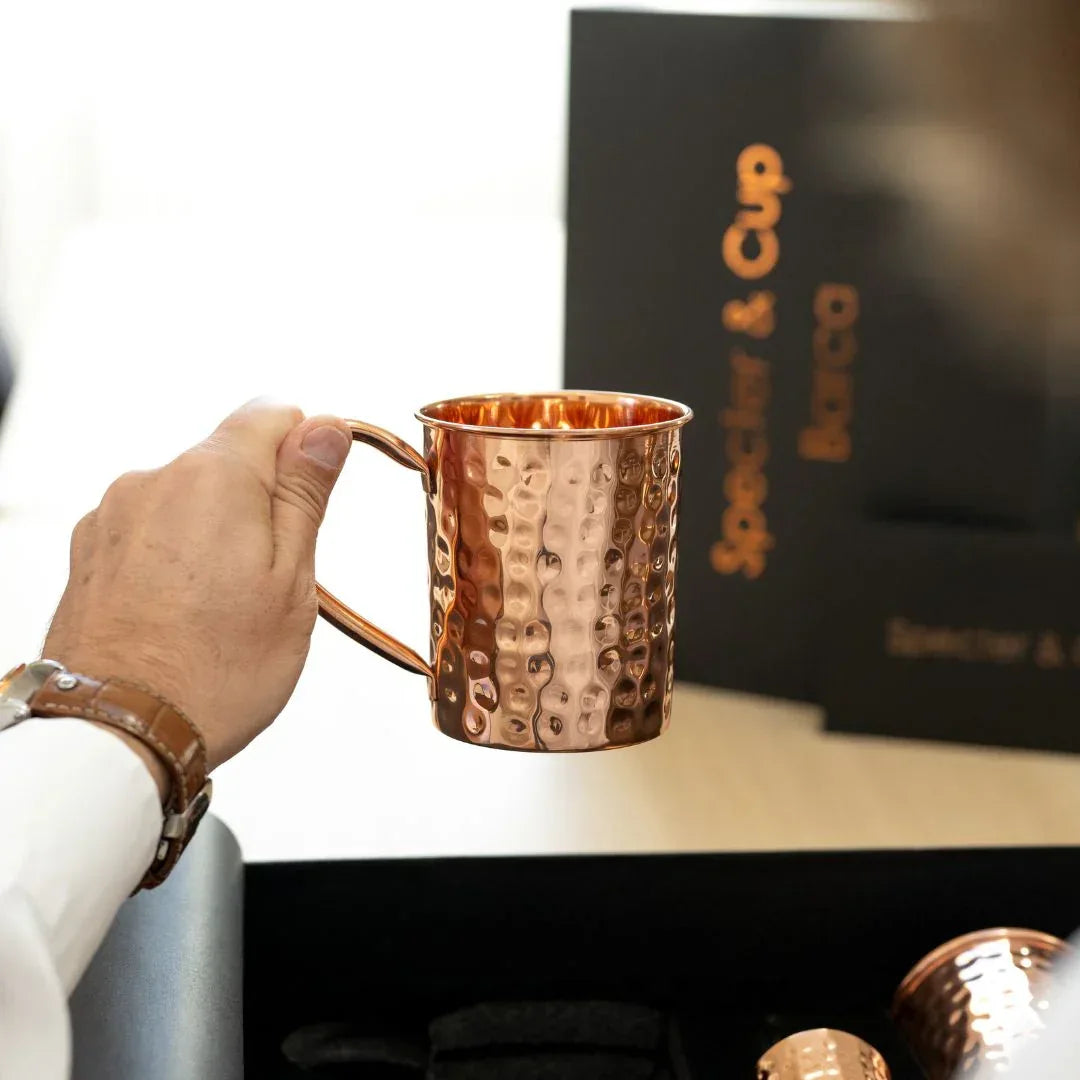 Gros plan d un mug en cuivre massif Barca tenu en main soulignant sa structure dense et son martelage manuel pour une experience authentique